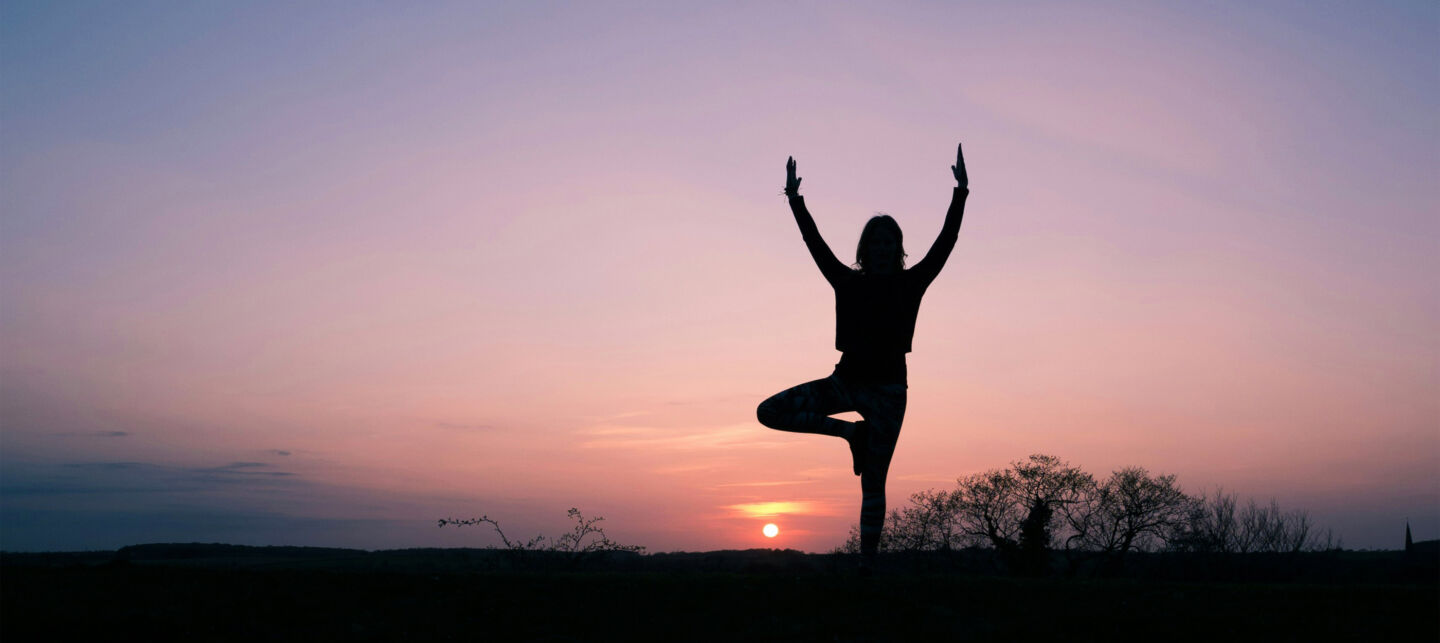Woman doing yoga silhouetted by the sunset.